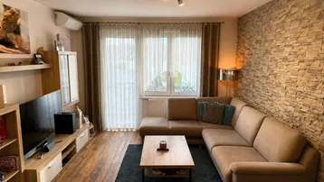 Gemütliches Wohnzimmer mit beiger Eckcouch, Holzboden und dekorativer Steinwand, hell und einladend.
