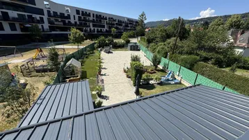 Blick von oben auf den Gemeinschaftsgarten mit Spielplatz, Gewächshaus und gepflasterten Wegen.