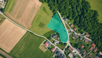 Luftaufnahme eines Grundstücks mit umliegenden Feldern, Wald und Wohnbebauung, das zum Verkauf steht.