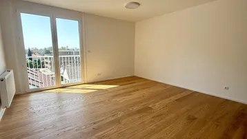 Helles Zimmer mit Holzboden und Zugang zu einem Balkon, bietet viel natürliches Licht.