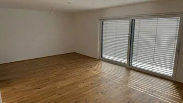 Helles Zimmer mit Holzboden und großer Schiebetür, die viel Tageslicht hereinlässt.