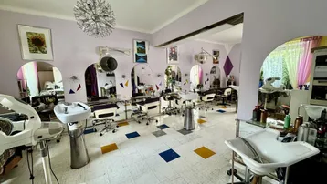 Geräumiger Friseursalon mit mehreren Styling-Stationen, Waschbecken und Fliesenboden in Lila und Weiß.