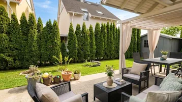 Möblierte Terrasse mit Pergola, umgeben von einem gepflegten Garten und hohen Hecken.