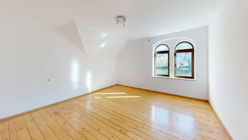 Helles Zimmer mit Holzdielenboden, Dachschräge und Rundbogenfenstern mit Blick ins Grüne.