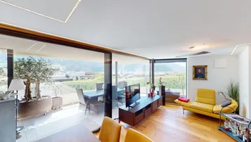 Gemütliches Wohnzimmer mit gelbem Sofa, Fernseher und Panoramablick auf Weinberge und Berge.