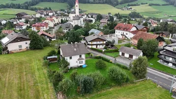 Übersichtsbild eines Wohnhauses mit Garten in einer ländlichen Umgebung, mit Blick auf ein nahegelegenes Dorf und Berge.