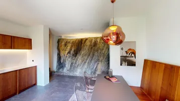Moderner Essbereich mit markanter Felswand, Holzelementen und einer Designleuchte.