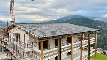 Neubau in Bauphase mit Dachziegeln, Gerüst und weitem Blick auf die umliegende Berglandschaft.