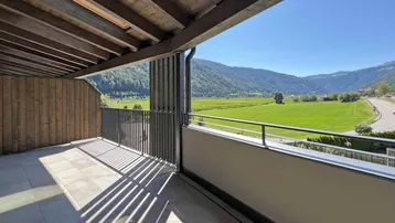 Geräumige Terrasse mit Holzbalkendecke, Fliesenboden und weitem Blick auf grüne Felder und Berge.