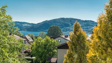 Panoramablick auf den See und die umliegenden Berge, umrahmt von grünen Bäumen und Häusern.