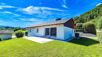 Modernes Einfamilienhaus mit großer Terrasse und gepflegtem Rasen in ländlicher Umgebung.