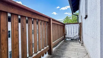 Rustikaler Holzbalkon mit Geländer und Blick auf die umliegende grüne Landschaft unter blauem Himmel.
