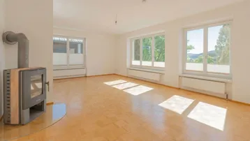 Helles Wohnzimmer mit Parkettboden, Kaminofen und großen Fenstern mit Blick ins Grüne.