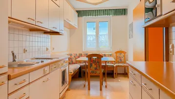 Helle Küche mit weiß-holzfarbenen Schränken, Essbereich und Fenster.