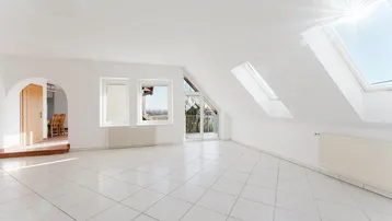 Helles, geräumiges Wohnzimmer im Dachgeschoss mit Fliesenboden, Dachfenstern und Zugang zum Balkon.