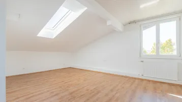 Helles Dachzimmer mit Schrägdach, Dachfenster und Laminatboden, gut belichtet.