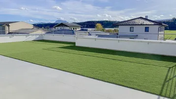 Weitläufige Dachterrasse mit Kunstrasen und Panoramablick auf die umliegende Landschaft und Berge.