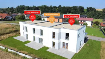 Luftaufnahme einer modernen Reihenhausanlage mit drei Einheiten, umgeben von grüner Landschaft.