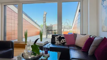 Helles Wohnzimmer mit bequemer Ledercouch, Blick auf die Dachterrasse und große Fensterfront.