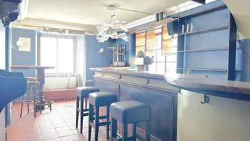 Innenansicht einer Bar mit blauen Wänden, Barhockern und einer Theke, die zum Verweilen einlädt.