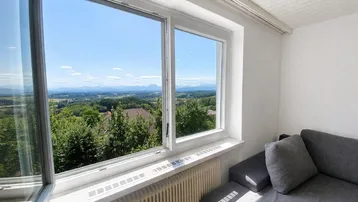 Helles Zimmer mit weitem Blick über die grüne Landschaft und die fernen Berge.
