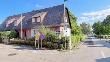 Ansicht des Hauses von der Straßenecke mit Mansarddach und umgebender Hecke.