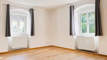 Helles Zimmer mit Parkettboden und zwei Fenstern, ideal als Wohn- oder Schlafzimmer nutzbar.