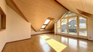 Helles Dachgeschosszimmer mit Holzbalkendecke, Parkettboden und großen Fenstern für viel Tageslicht.