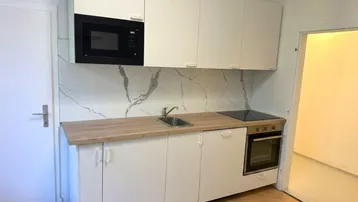 Kleine moderne Küche mit weißen Schränken, Holzarbeitsplatte und integrierten Geräten.