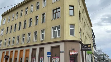 Eckgebäude mit gelber Fassade und Mansarddach in städtischer Umgebung.