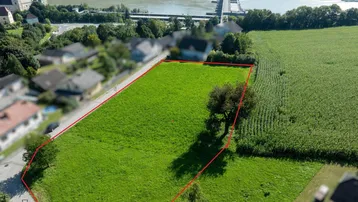 Luftaufnahme eines grünen Grundstücks mit roter Umrandung, umgeben von Häusern und Natur.