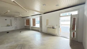 Geräumiger, leerstehender Geschäftsraum mit großen Fenstern und Holzdeckenverkleidung, bereit zur individuellen Gestaltung.