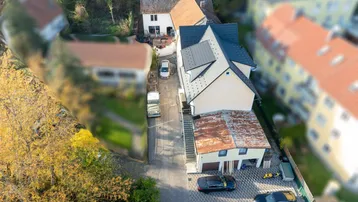 Luftaufnahme eines modernen Wohnhauses mit Garagen, gepflastertem Vorplatz und umgeben von viel Grün.