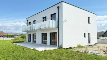 Modernes weißes Gebäude mit Balkonen und einer Terrasse auf einem unbebauten Grundstück.
