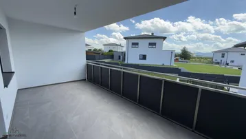 Geräumiger Balkon mit modernen Fliesen und Blick auf die umliegenden Neubauten und die Landschaft.