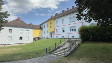 Außenansicht eines Mehrfamilienhauses mit weißer Fassade und grüner Umgebung.