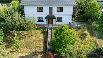Freistehendes Einfamilienhaus mit weißer Fassade und dunklem Dach, umgeben von viel Grün.