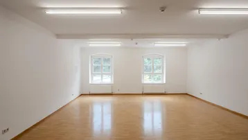 Heller, leerer Raum mit Parkettboden und zwei großen Fenstern, ideal für Büro oder Gewerbe.