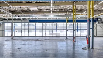 Geräumige Industriehalle mit hohen Decken, Betonboden und großen Fenstern, die viel Tageslicht hereinlassen.