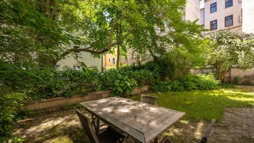 Ruhiger Innenhofgarten mit Holztisch und Stühlen, umgeben von üppigem Grün und Bäumen.