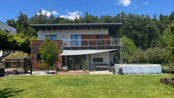 Modernes Haus mit großem Garten, Terrasse, Balkon und einem Aufstellpool unter blauem Himmel.