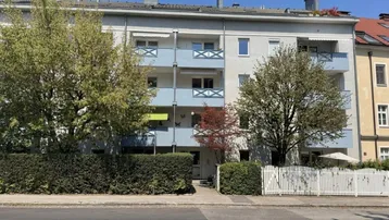 Mehrfamilienhaus mit Balkonen und gepflegter Hecke an der Vorderseite unter blauem Himmel.