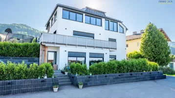 Modernes Wohnhaus mit Balkon, gepflegter Hecke und Bergblick.