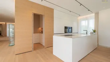 Moderne Küche mit weißen Schränken, Kochinsel und integrierten Holzschränken in minimalistischem Design.