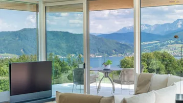 Helles Wohnzimmer mit bodentiefen Fenstern, modernem Sofa und atemberaubendem See- und Bergblick.