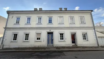 Fassade eines Mehrfamilienhauses mit mehreren Fenstern und zwei Eingangstüren an einer Straße.