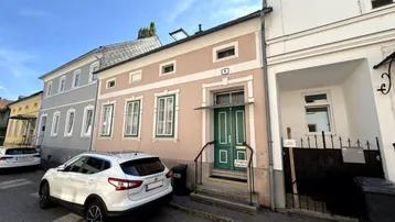 Fassade eines Wohnhauses von der Straße aus gesehen mit einem geparkten Auto davor.
