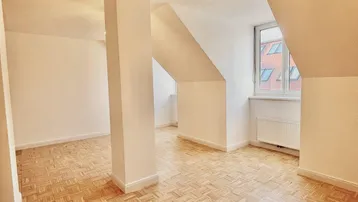 Helles Dachgeschosszimmer mit Parkettboden, schrägen Wänden und einem Fenster.
