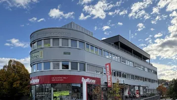 Modernes Geschäftsgebäude mit geschwungener Fassade und großen Fenstern unter einem dynamischen Himmel.