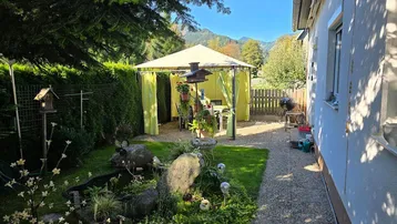 Gepflegter Gartenbereich mit Pavillon, Teich und Bergblick, ideal für entspannte Stunden im Freien.